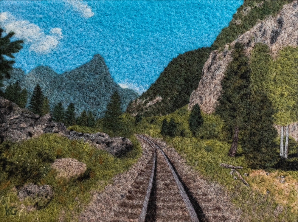 A two-dimensional felted wool landscape of a railroad near mountains.